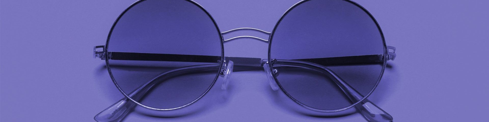 A pair of round ‘John Lennon’ style purple-tinted spectacles on a purple background.